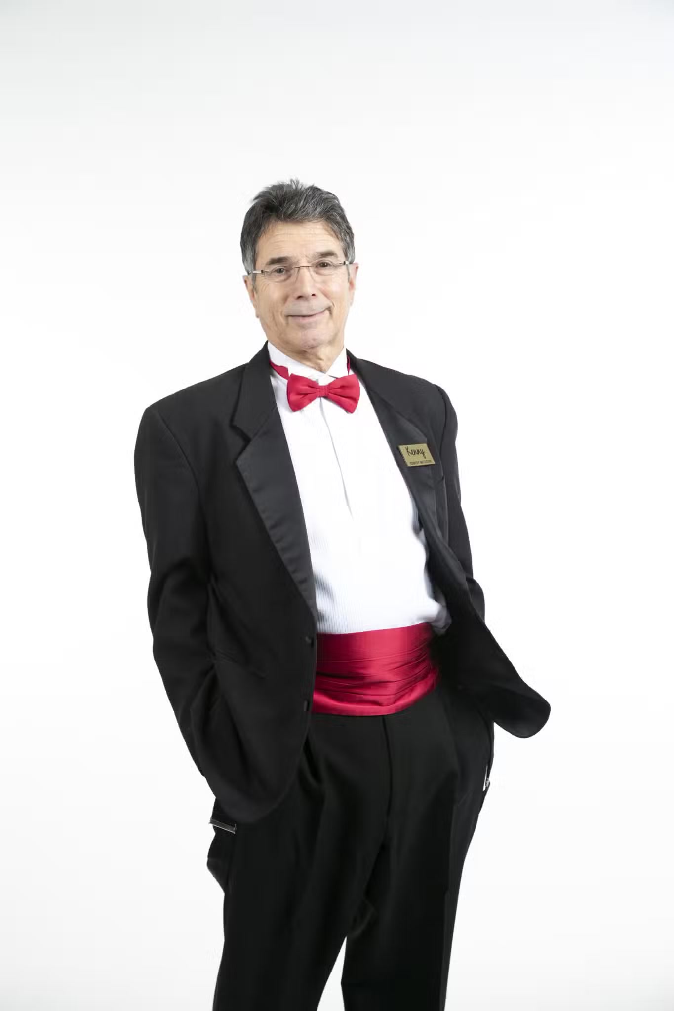 Ken Caplan smiling in his signature tuxedo and red bow tie